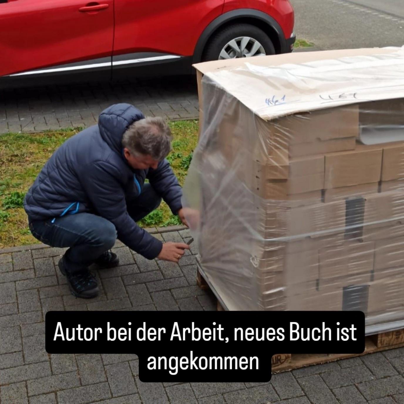 Der Autor in einer blauen Jacke hockt vor einer Palette von Büchern, während er die Versandfolie entfernt